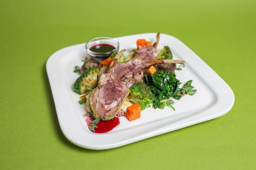 A delicious and healthy rib dish with mushrooms, broccoli, carrots and spinach on a white plate on a green background.