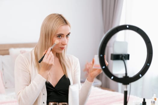 Young woman making beauty and cosmetic tutorial video content for social media. Beauty blogger smiles to camera while showing how to apply mascara to audience or followers. Blithe