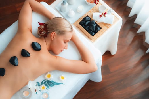 Panorama top view hot stone massage at spa salon in luxury resort with day light serenity ambient, blissful woman customer enjoying spa basalt stone massage glide over body. Quiescent