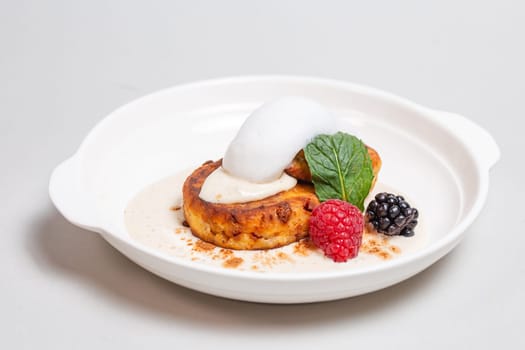 Gourmet cottage cheese pancakes with berries on white plate on white background. Delicious breakfast food.