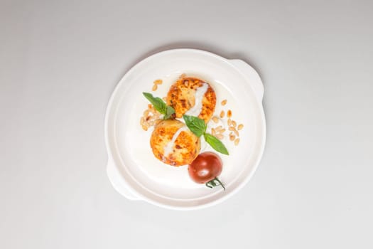 Two round fried cheese pancakes with sour cream and cherry tomatoes on a white plate on a white background. Isolated on a white background.