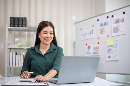 Beautiful determined business woman working using laptop and calculator calculating turnover in modern office.