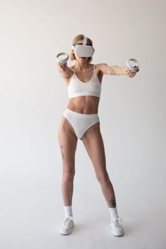 Beautiful thin girl in white shorts and a top in a virtual reality helmet posing on a white background. High quality photo