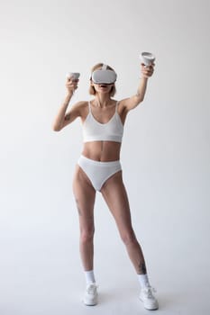 Beautiful thin girl in white shorts and a top in a virtual reality helmet posing on a white background. High quality photo