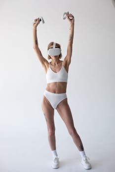 Beautiful thin girl in white shorts and a top in a virtual reality helmet posing on a white background. High quality photo