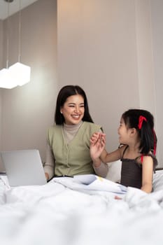 Mom work from home with children. Mother working on bed laptop in bedroom with child daughter. Funny authentic lifestyle family moment.