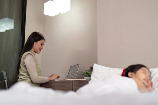 Asian mother working on bed with sleeping daughter by side at home.