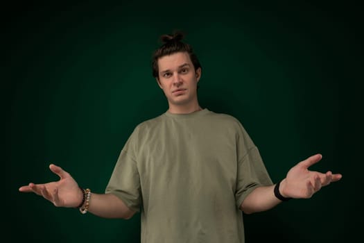 A man is standing in front of a green wall, extending both of his hands outwards. He appears to be in a posture of offering or greeting.