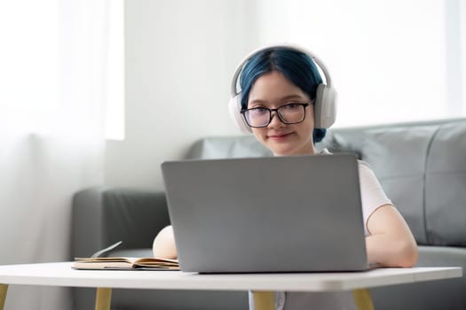 Happy young woman teenage wearing headphones writing note. student online learning class study online video call zoom teacher with laptop and book.