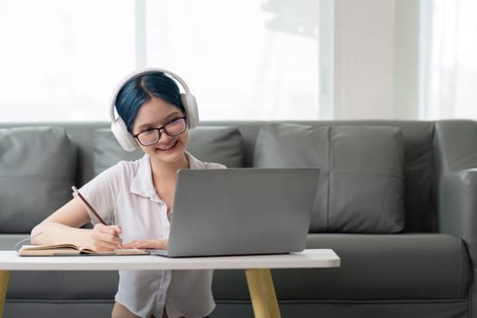 Happy young woman teenage wearing headphones writing note. student online learning class study online video call zoom teacher with laptop and book.