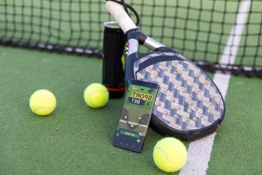 A tennis ball, a racket and a mobile phone with a put screen lie on a blue background. The concept of advertising a tennis club or ordering services. Horizontal photo. High quality photo