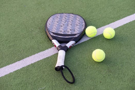 Yellow balls on grass turf near padel tennis racket behind net in green court outdoors with natural lighting. Paddle is a racquet game. Professional sport concept with copy space. High quality photo
