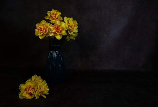 a still life with a blue vase with yellow daffodils with an orange heart on a dark background