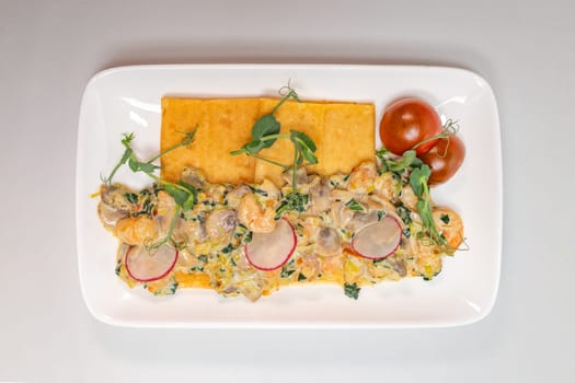 A savory crepe filled with seafood and vegetables, topped with a creamy sauce and served on a white plate.