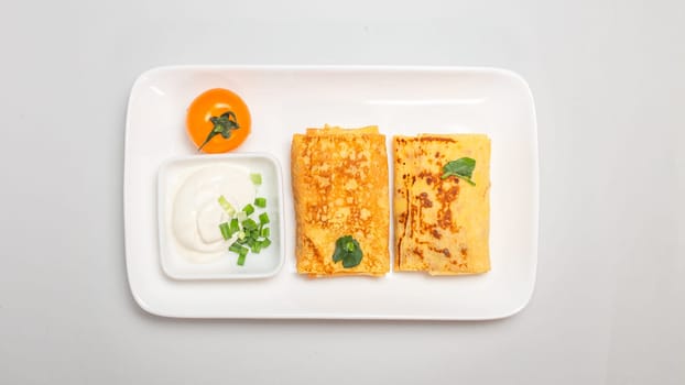 Two folded stuffed savory crepes with sour cream and chives garnish on a white plate on a white background.