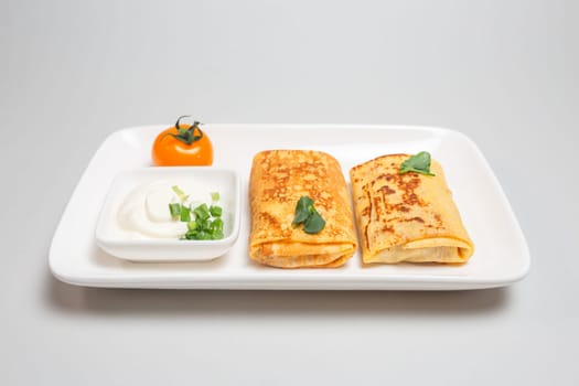 Two folded stuffed savory crepes with sour cream and chives garnish on a white plate on a white background.