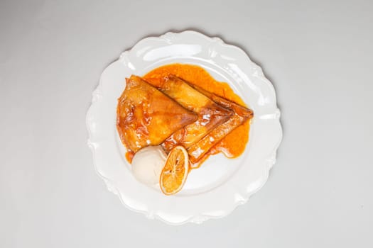 A decadent dessert of crepes topped with orange sauce and a scoop of vanilla ice cream, isolated on a white background.