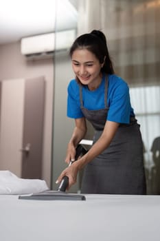 Cleaning service employee removing dirt from with professional equipment. Female housekeeper cleaning the mattress on the bed with vacuum cleaner.