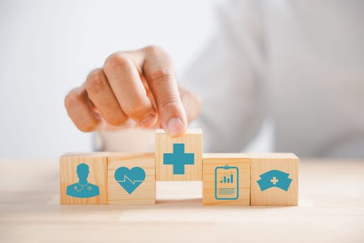 Captured in an image, Hand clutches wooden block featuring healthcare and medical icons. Reflects safety, health, and family well-being, symbolizing pharmacy and heart care. health care concept