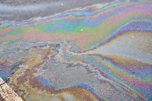 Fuel stain on wet asphalt. Colored stains from a gasoline leak on the road. Environmental pollution concept.