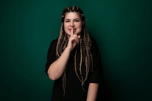 A woman with long dreadlocks is standing in front of a green wall. She appears confident and stylish, showcasing her unique hairstyle.