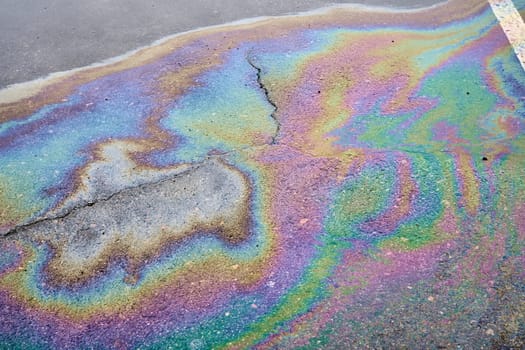 Oil stains from leaks in the car engine. Oil after rain makes spots with rainbow reflections refractive sun spectrum. Beautiful color mosaic, abstraction, ecology