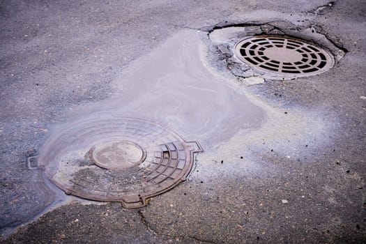 The oil slick on the asphalt road is contributing to water pollution as it drains into the storm drain