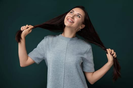 A woman with long hair stands in front of a solid green background. She appears confident and poised, with her hair flowing down her back. The color contrast between her hair and the background creates a striking visual impact.