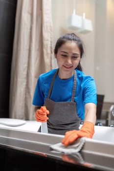 Professional cleaning service company employee in rubber gloves cleaning and detergent spray in bathroom.