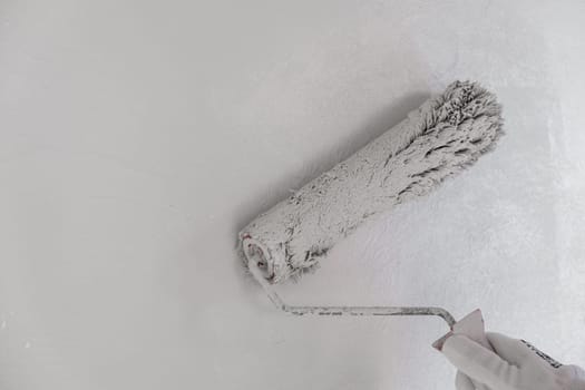 Painting the wall with a roller with white paint. Painting a bare wall with a roller with white paint. Apartment painting, renovation using white paint