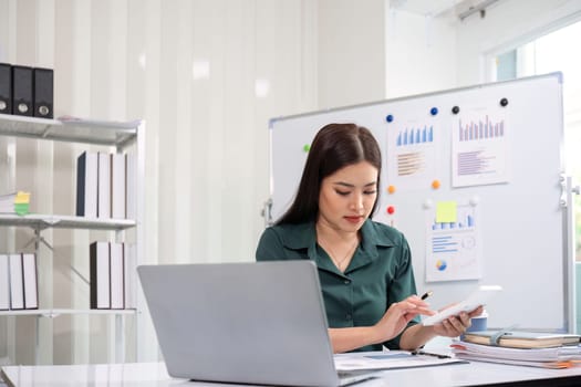 Beautiful determined business woman working using laptop and calculator calculating turnover in modern office.