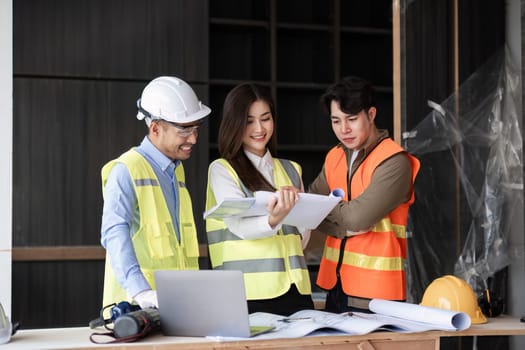 civil engineers meet to plan a construction project and brainstorm ideas about how to work through paper plans and records with laptop