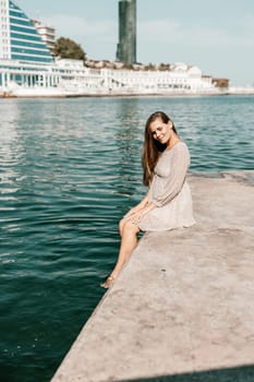 A woman is sitting in the water wearing a white dress. The water is calm and blue. The woman is enjoying the moment and taking in the beauty of the scene