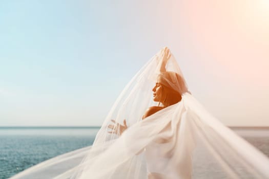 A woman stands on a beach with a white veil over her head. The scene is serene and peaceful, with the woman's gaze directed towards the water