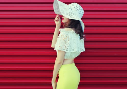 Beautiful young woman model posing in white summer straw hat on pink background