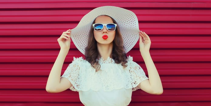 Beautiful young woman model posing in white summer straw hat on pink background