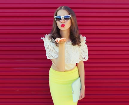 Beautiful young woman model blowing kiss posing with handbag clutch on pink background
