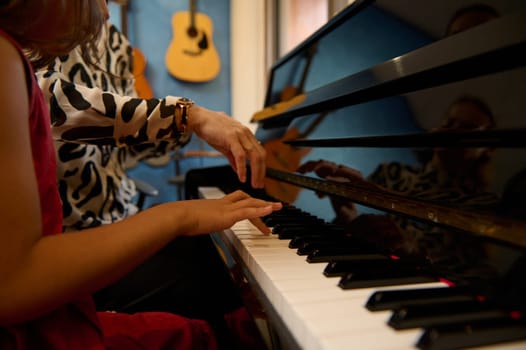 Close-up view of the hands of a musician teacher and girl fingers touching the piano keys, explaining the true positions of fingers while learning play piano and capturing the rhythm of music