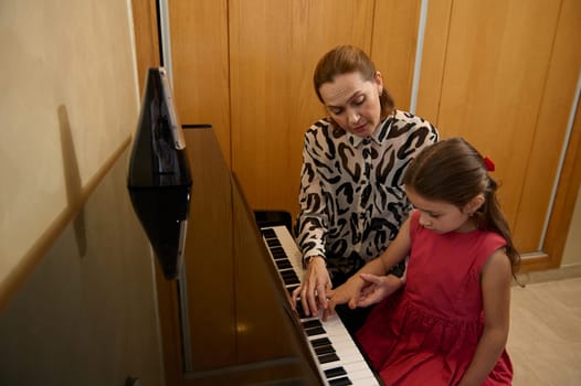 School age little pianist girl plays piano, composing a melody under the guidance of her teacher during individual music lesson at home. Children. Education. Lifestyles. Hobbies and entertainment