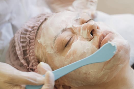 A woman is having a facial mask applied to her face in a spa setting. The skincare professional is gently smoothing on the mask for a revitalizing treatment.