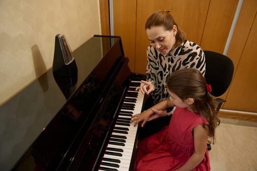 Beautiful little pianist girl is playing piano, composing a melody under the guidance of her teacher during individual music lesson at home. Children. Education. Lifestyles. Hobbies and entertainment