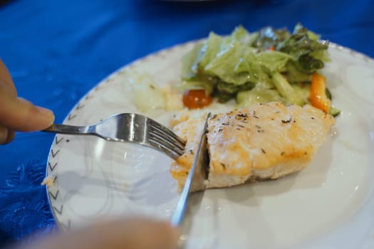 A piece of grilled salmon seasoned with herbs on a white plate accompanied by a fresh green salad, ready for a healthy meal.