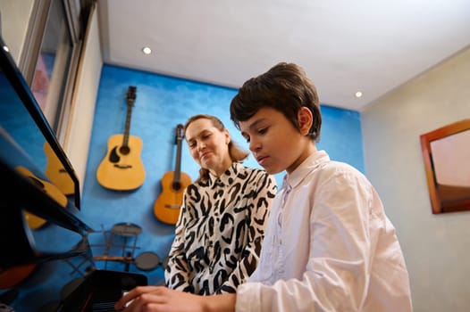 Talented teenager boy musician having a piano lesson with his teacher. Female pianist explaining the correct position of hands on piano keys. Musical education and talent development in progress