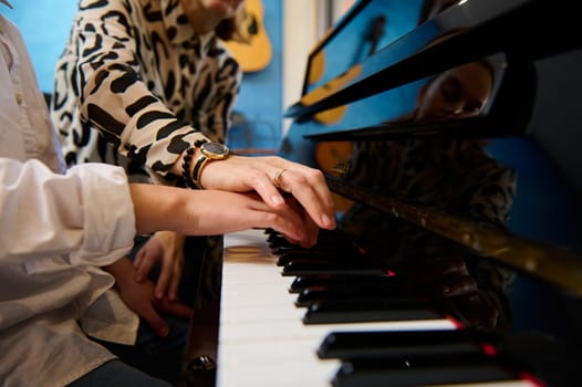Closeup female musician pianist teaching a teenager student boy the correct position of fingers, sitting at piano while performing musical composition on grand pianoforte, during music lesson.