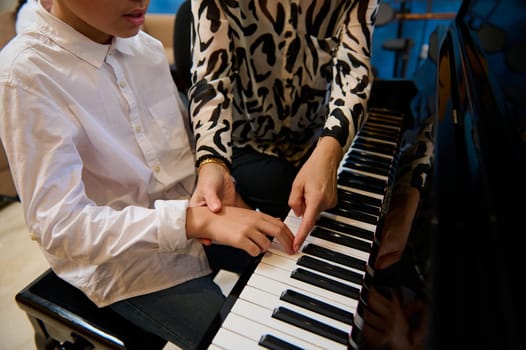 Close-up shot of a female pianist, music teacher explaining correct hands and finger position on piano keys, teaching piano lessons at home. Create music and songs concept. Leisure and hobby indoors.
