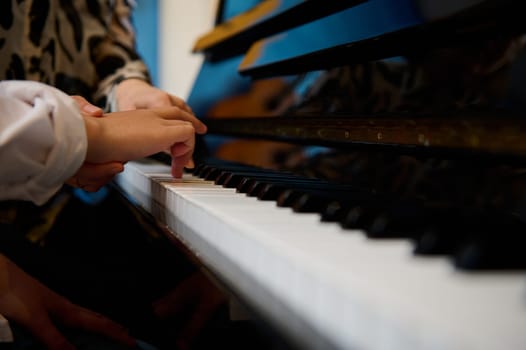 Side view hands of musician pianist teacher maestro teaching a child boy the true position of fingers on piano keys while performing musical composition on grand pianoforte, during music piano lesson