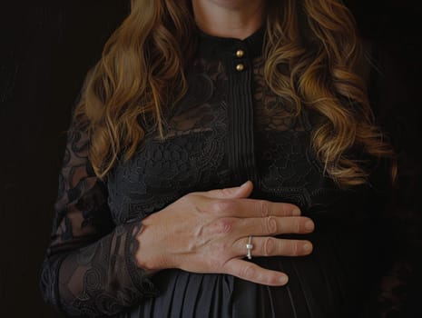 A pregnant woman stands gracefully in a black dress, her hands delicately clasped together in front of her.