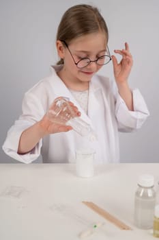 A Caucasian girl in glasses and a white coat does chemical experiments on a white background. Vertical photo