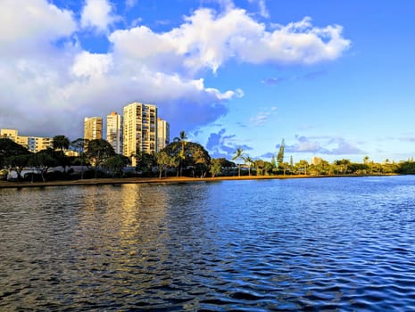 Serene beauty of the Ala Wai Canal during the golden hour. In this mesmerizing photograph, the tranquil waters reflect the radiant hues of the sky, while modern buildings stand tall in the backdrop, showcasing a harmonious blend of natural beauty and urban architecture.