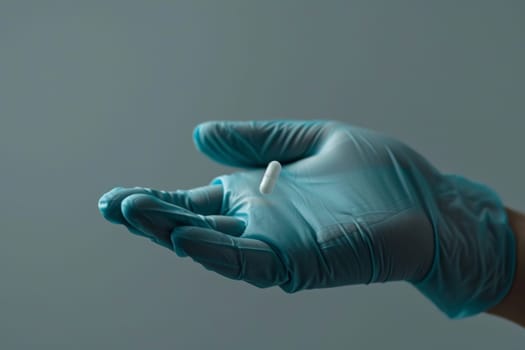 A close-up shot of a healthcare worker's hand in a blue glove, holding white capsule, against a blue backdrop